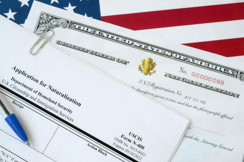 N-400 Application for Naturalization and Certificate of naturalization lies on United States flag with blue pen from Department of Homeland Security n-400 and certificate of naturalization